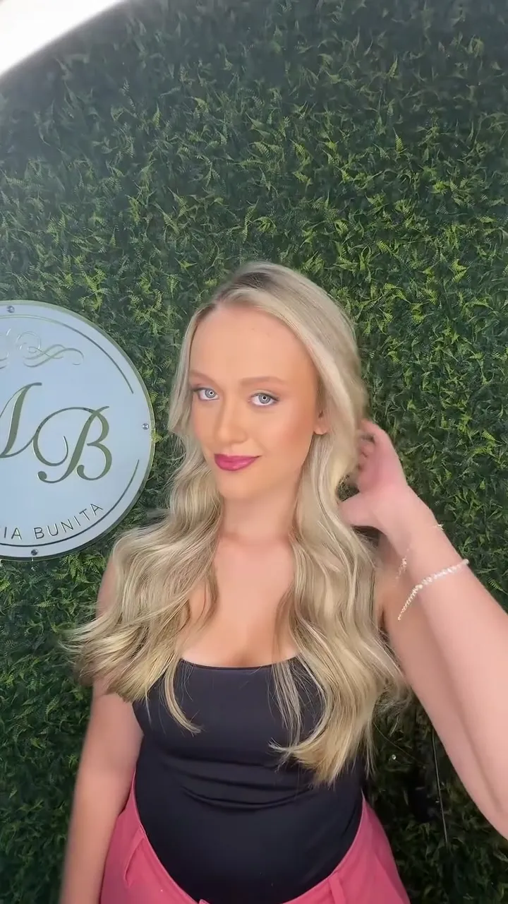 Cliente loira ao lado do espelho redondo com o monograma MB, na parede verde do salão